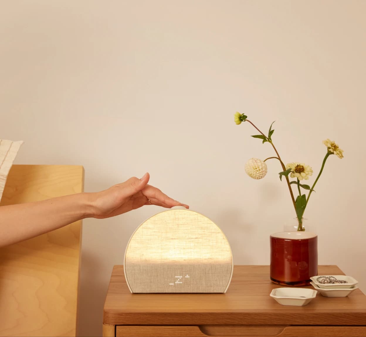 Hand tapping the top button on a Hatch Restore 3 sitting on a nightstand